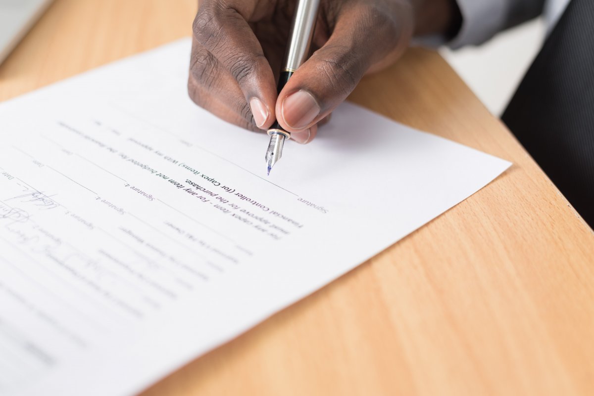 photograph of a hand with a pen signing a document