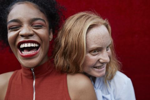 close up of young women laughing while standing against red wall